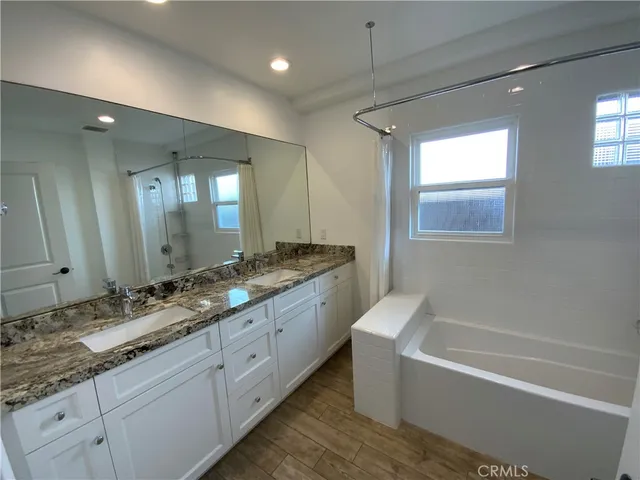 a bathroom with a granite countertop double vanity sink and mirror with bathtub