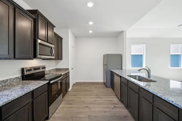 a kitchen with granite countertop stainless steel appliances a sink dishwasher stove top oven and wooden cabinets