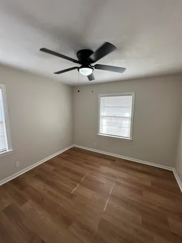 an empty room with wooden floor ceiling fan and windows