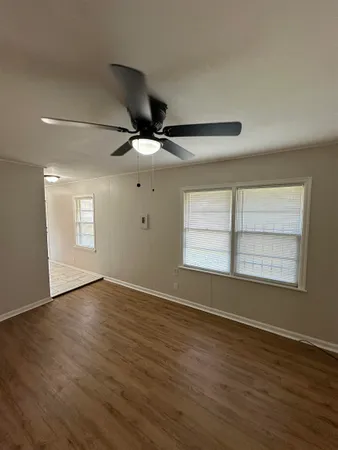 an empty room with wooden floor fan and windows