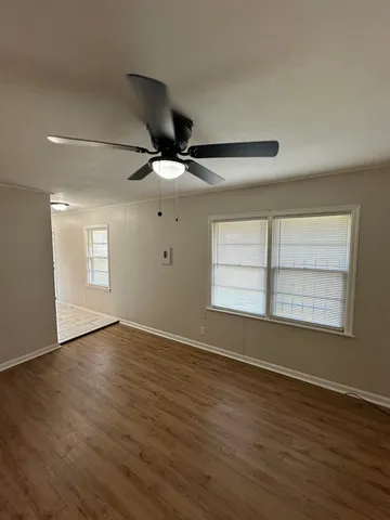 an empty room with wooden floor fan and windows