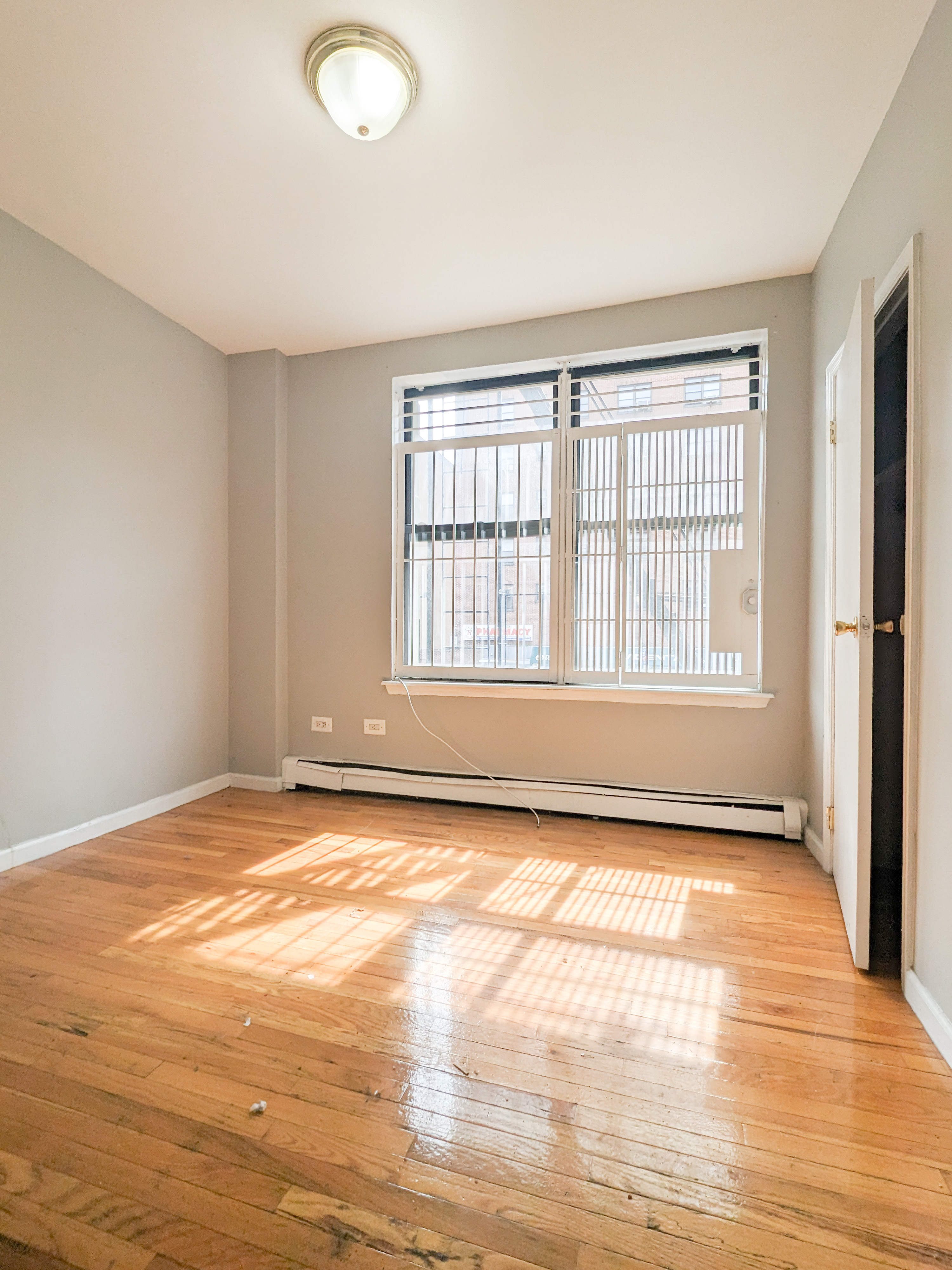 a view of an empty room with window and hardwood floor