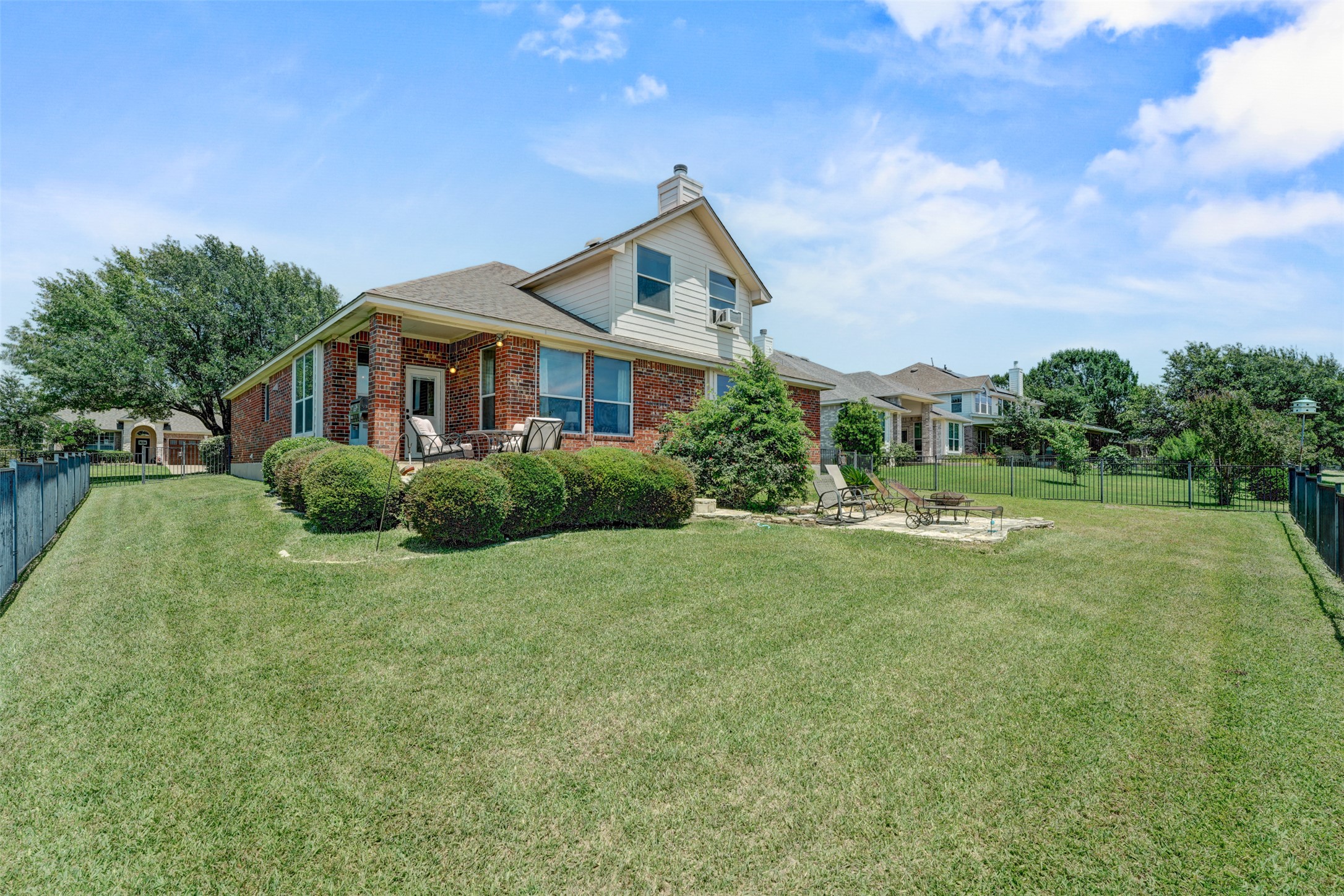 2521 Amen Corner Road Pflugerville, TX 78660 - Photo 36 of 40 Expansive green lawn with a covered patio, brick exterior, multiple windows, and a black metal fence