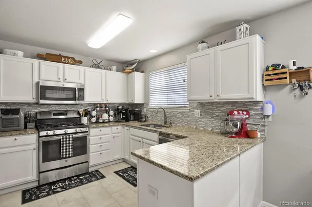 a kitchen with stainless steel appliances granite countertop a sink dishwasher stove and white cabinets with wooden floor