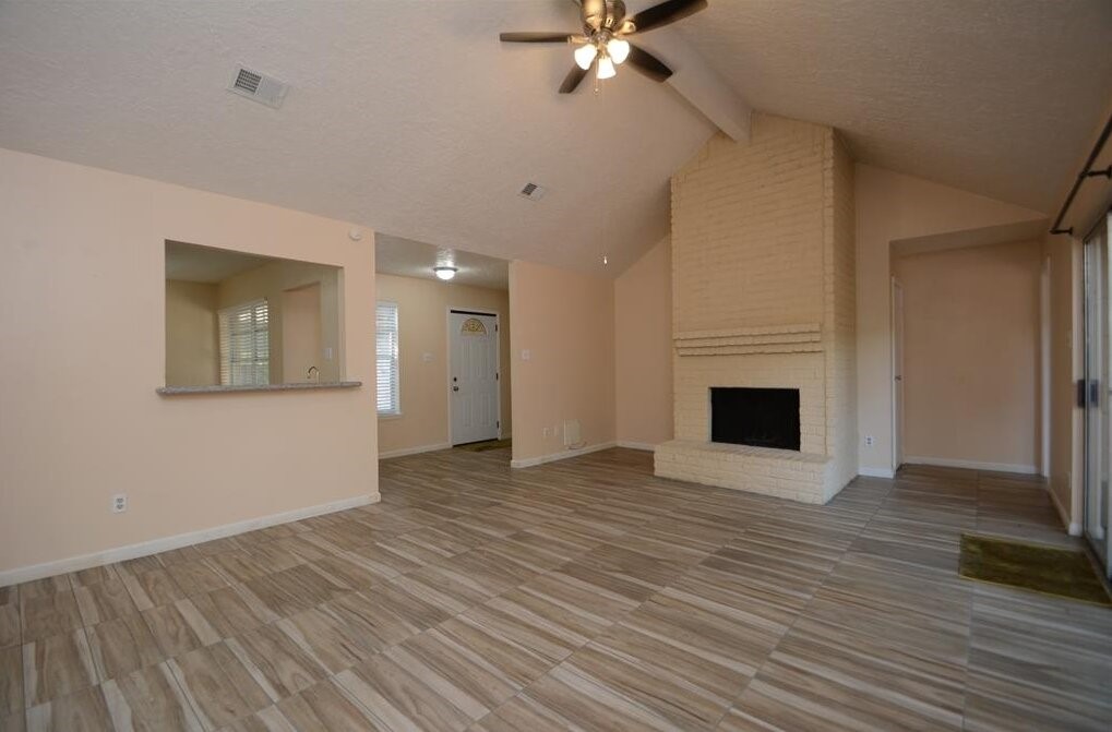 15 South Tallowberry Drive Spring, TX 77381 - Photo 6 of 26 Bright living room with vaulted ceilings, ceiling fan, brick fireplace, tile flooring, and an open pass-through to the kitchen.