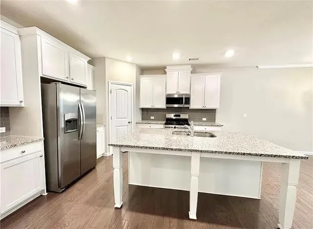 a kitchen with kitchen island granite countertop a stove a sink and a refrigerator with wooden floor