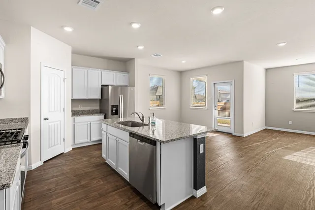 a kitchen with stainless steel appliances granite countertop a stove top oven a refrigerator a sink and dishwasher with wooden floor