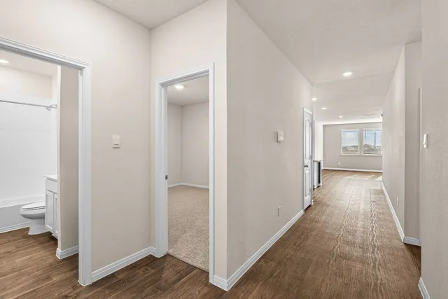 a view of a hallway with wooden floor and a bathroom
