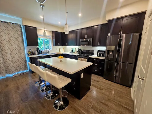 a kitchen with stainless steel appliances a refrigerator a sink dishwasher a stove and a dining table with wooden floor