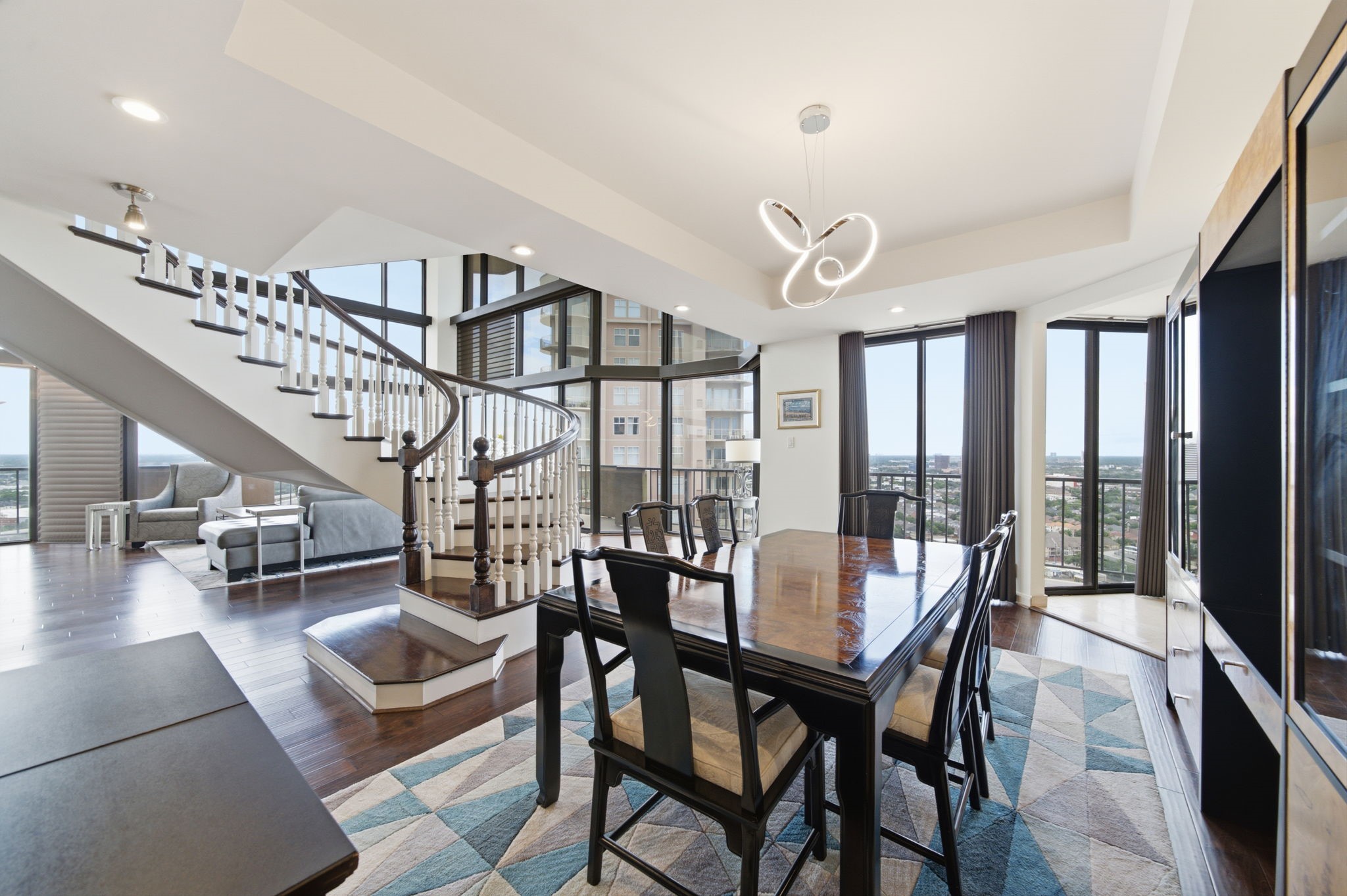 3350 McCue Road, Unit 2402 Houston, TX 77056 - Photo 20 of 49 Framed by towering two-story windows and an architectural curved staircase, the formal dining room sets an elegant stage for hosting. Rich hardwood flooring flows beneath an artful contemporary chandelier, while expansive glass doors open out to a private balcony overlooking panoramic city horizons.