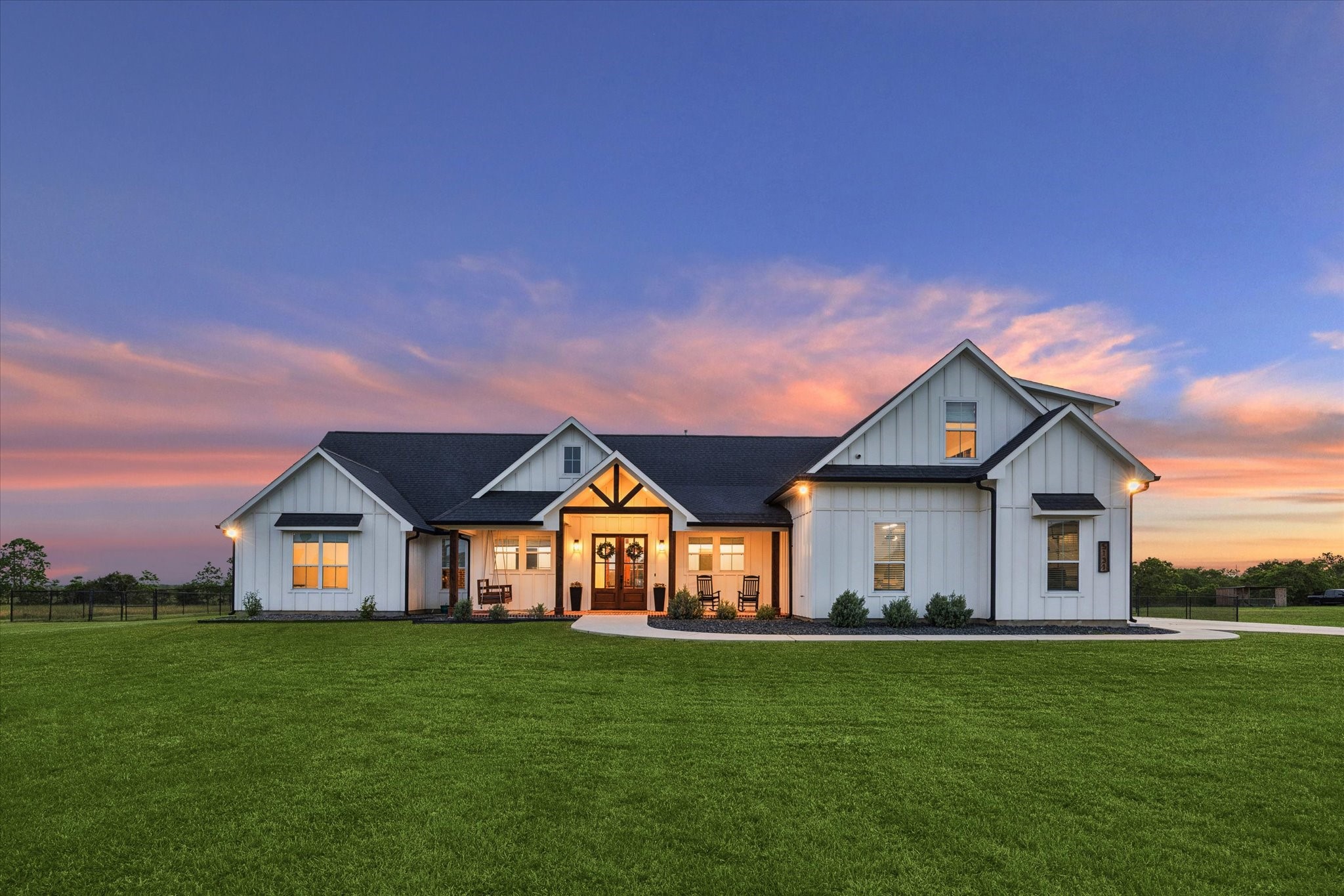 Modern farmhouse-style home with a spacious, well-maintained lawn. The house features a white exterior with black trim, large windows, and a welcoming front porch.