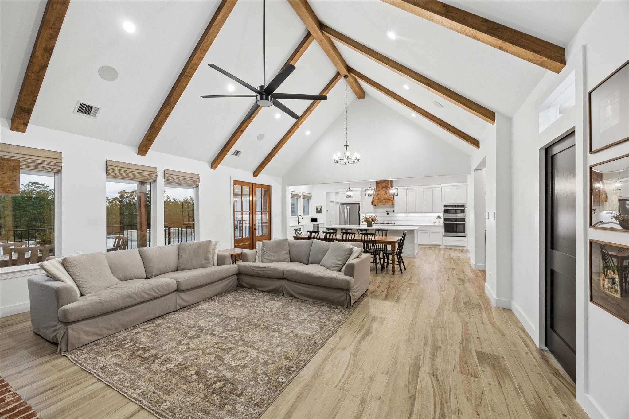 5131 Timber Ridge Drive Sealy, TX 77474 - Photo 12 of 50 Vaulted ceiling with exposed wooden beams, a modern ceiling fan, and abundant natural light. The room seamlessly connects the cozy seating area to a stylish kitchen with a large island, perfect for entertaining.