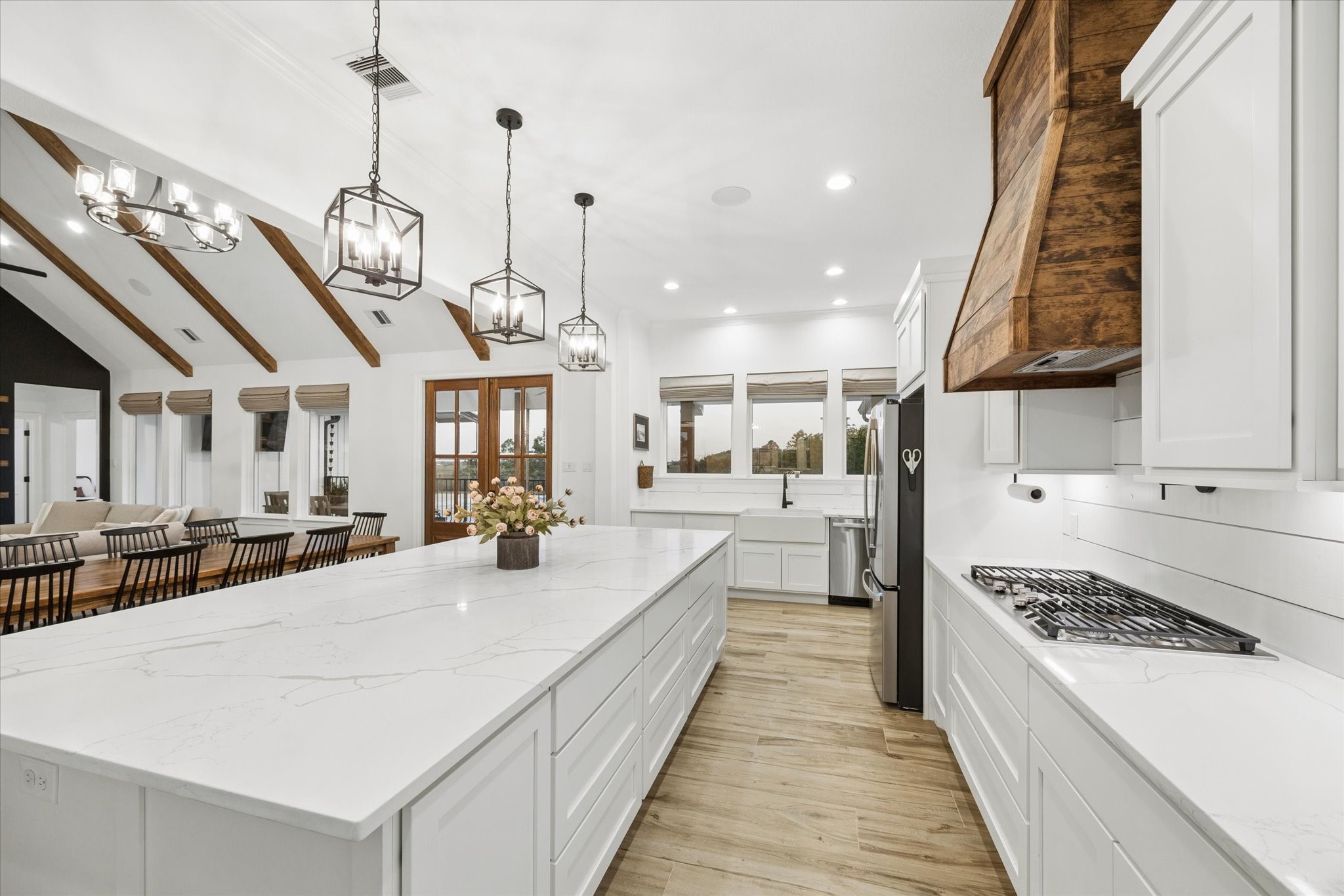 5131 Timber Ridge Drive Sealy, TX 77474 - Photo 14 of 50 Spacious, modern kitchen with a large marble island, white cabinetry, and wood accents. It features elegant pendant lighting, a farmhouse sink, and a cozy dining area with a vaulted ceiling and exposed beams, creating a bright and inviting space.