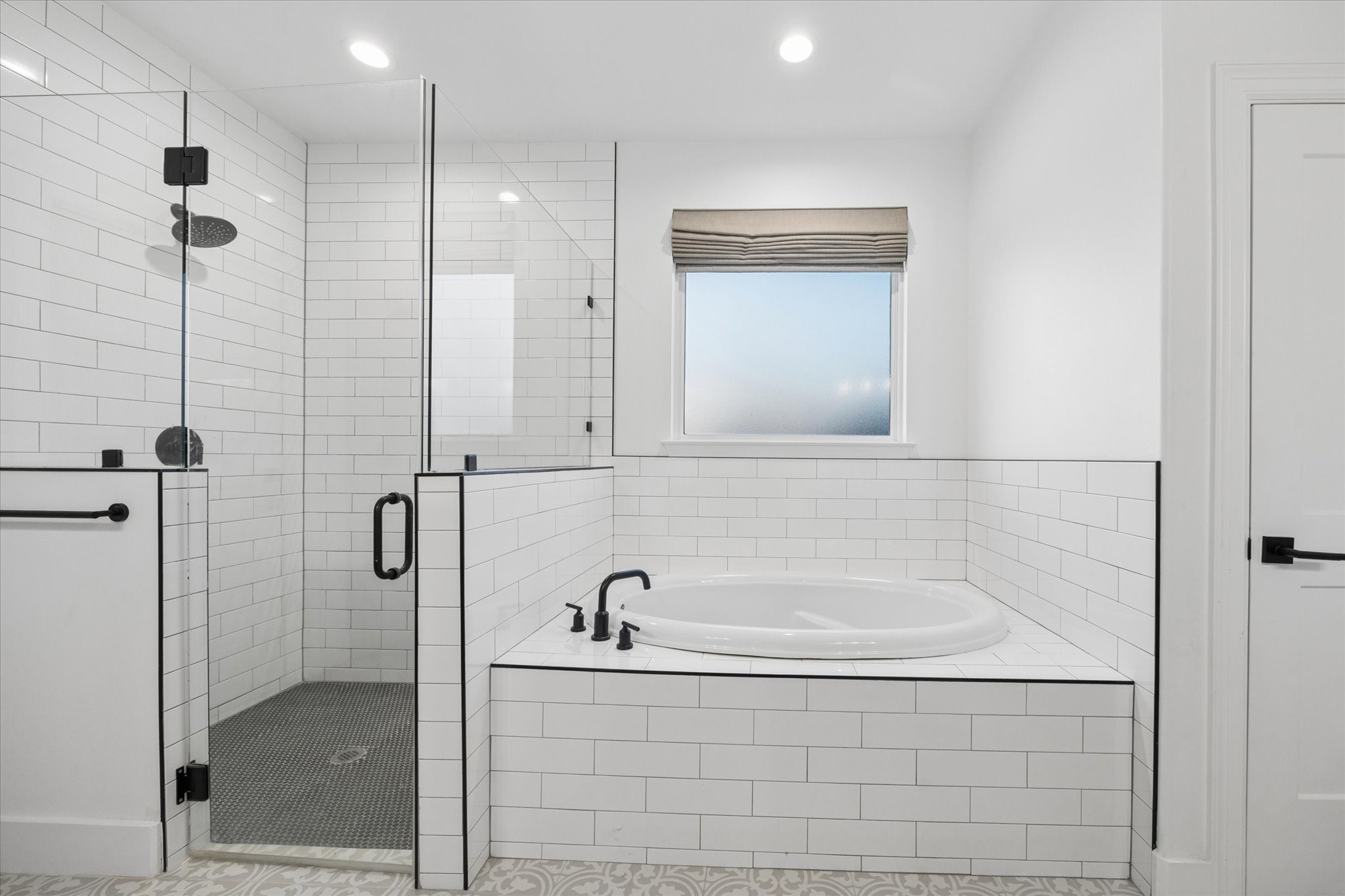 5131 Timber Ridge Drive Sealy, TX 77474 - Photo 24 of 50 This bathroom features a spacious glass-enclosed shower and a sleek soaking tub, both accented by white subway tiles. The room is bright with recessed lighting and a window with a shade for privacy.