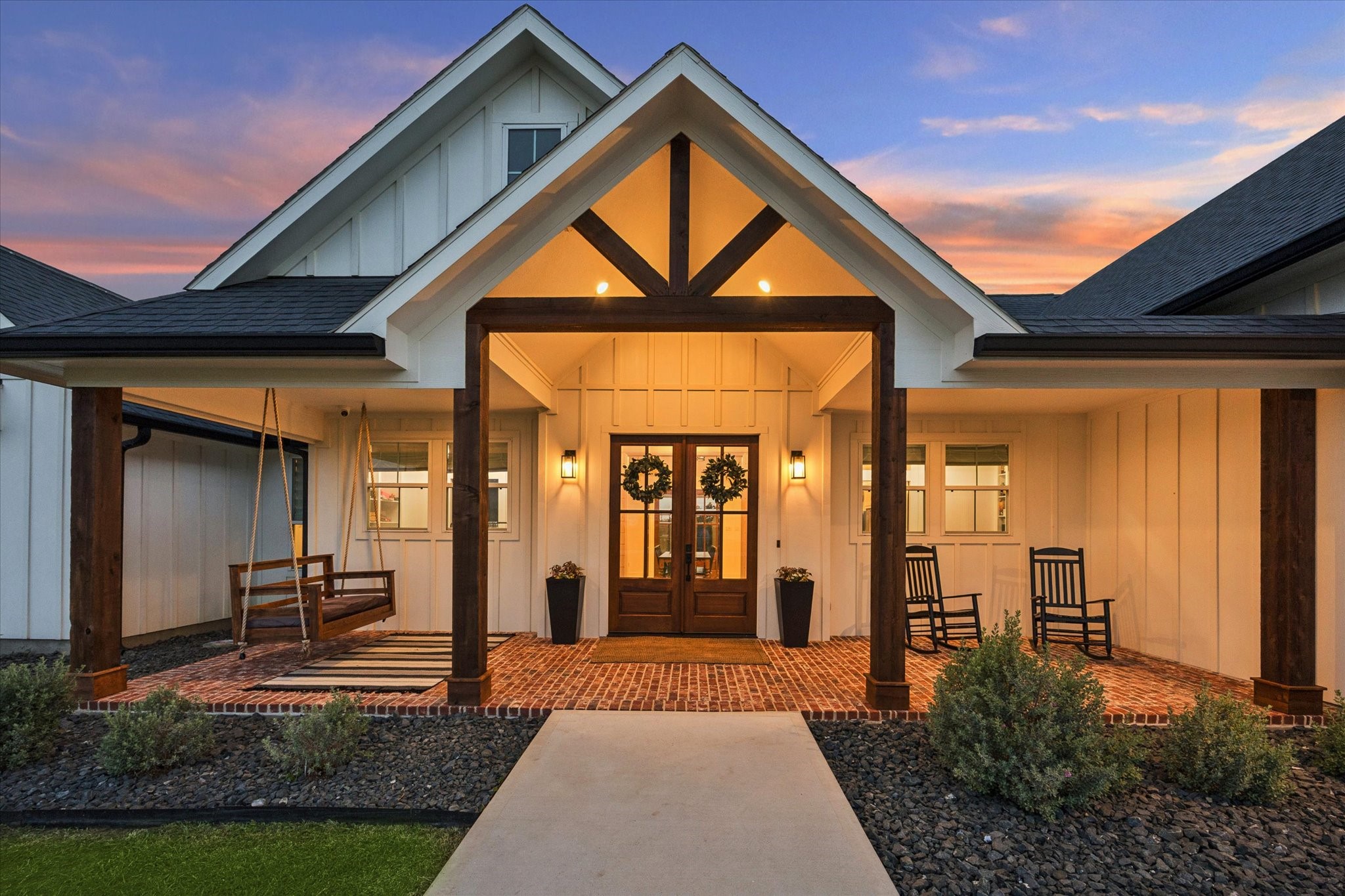 5131 Timber Ridge Drive Sealy, TX 77474 - Photo 3 of 50 Charming modern farmhouse with a welcoming front porch featuring a swing and warm lighting. The exterior showcases a gabled roof, board and batten siding, and a stylish brick porch.