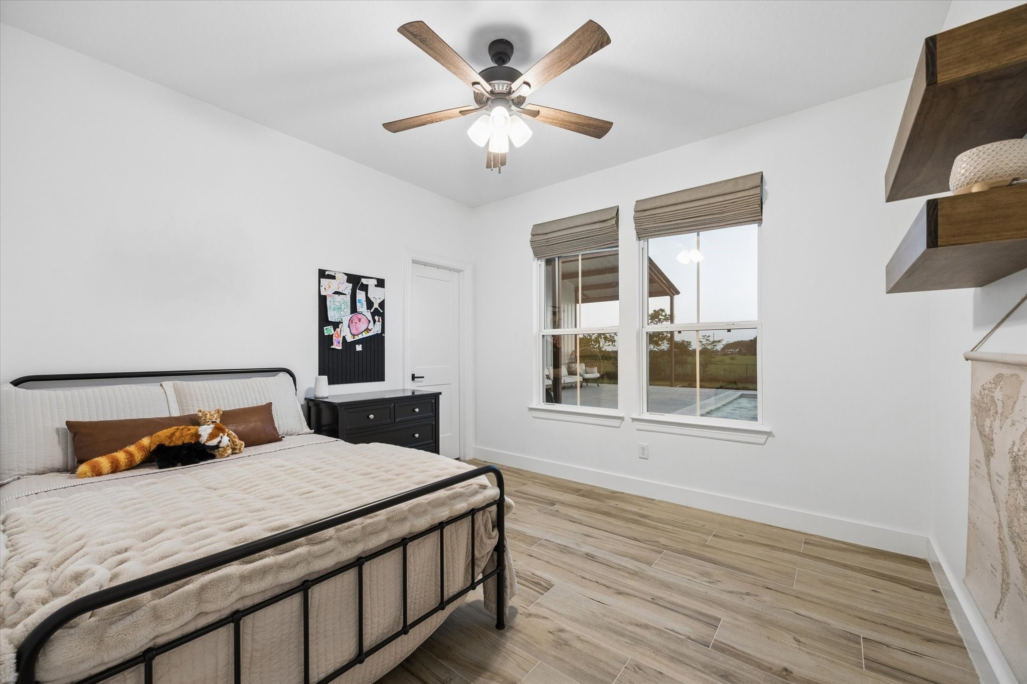 5131 Timber Ridge Drive Sealy, TX 77474 - Photo 33 of 50 This bedroom features a modern aesthetic with wood-look flooring and a ceiling fan. It has large windows offering natural light and a view of the backyard.