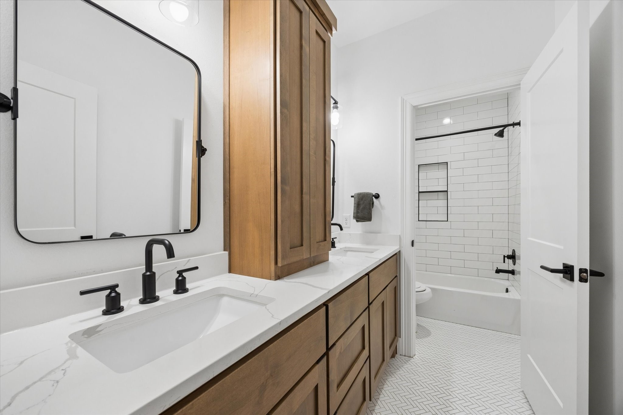 5131 Timber Ridge Drive Sealy, TX 77474 - Photo 35 of 50 This bathroom features a modern double vanity with black fixtures, a sleek marble countertop, and ample wooden cabinetry. The room is bright with a clean white tile floor and a shower-tub combo with subway tile walls.