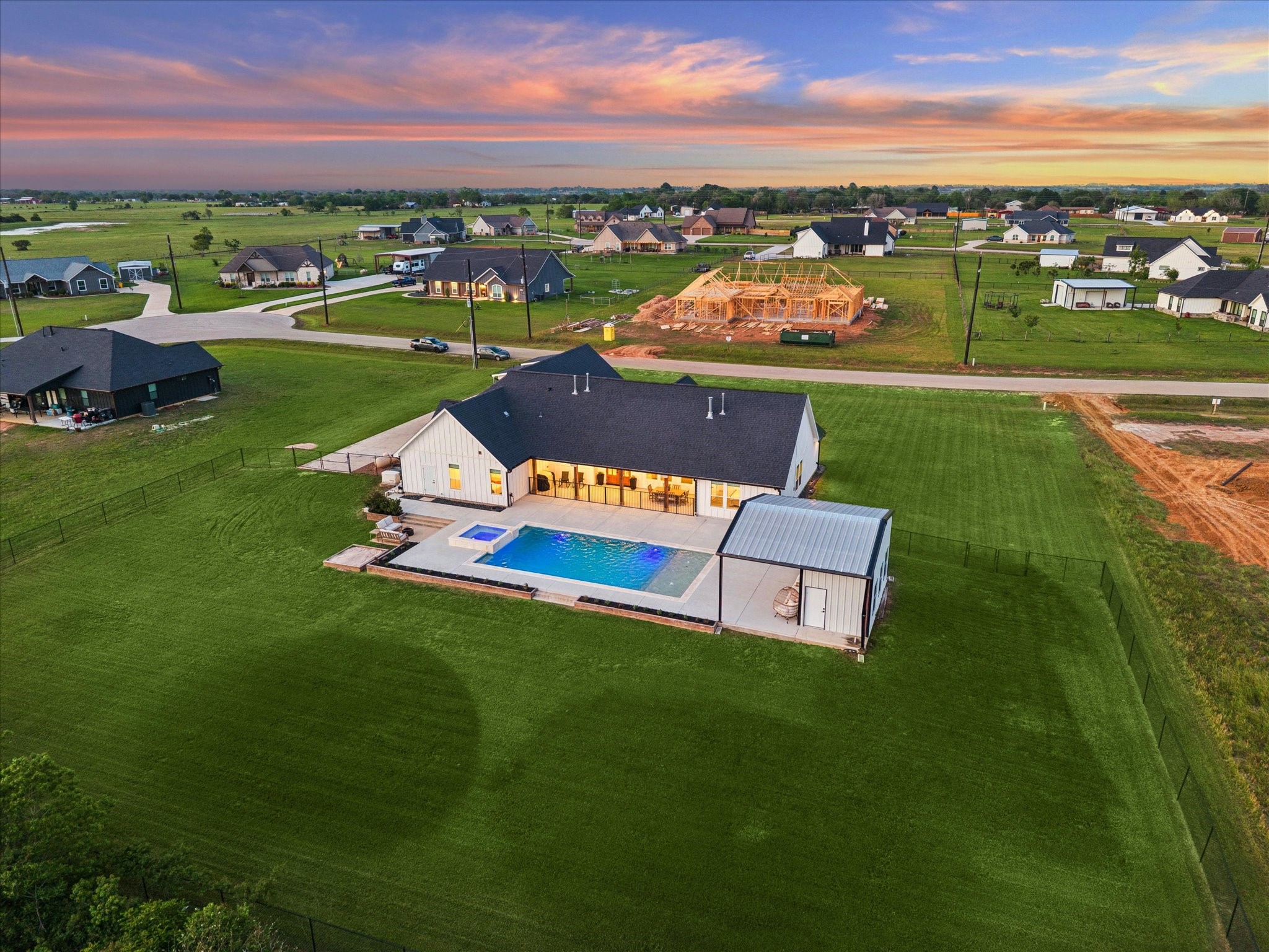 5131 Timber Ridge Drive Sealy, TX 77474 - Photo 49 of 50 This photo showcases a modern single-story home with a spacious backyard, featuring a swimming pool and a covered patio. It's set in a peaceful neighborhood with ample green space and nearby homes.