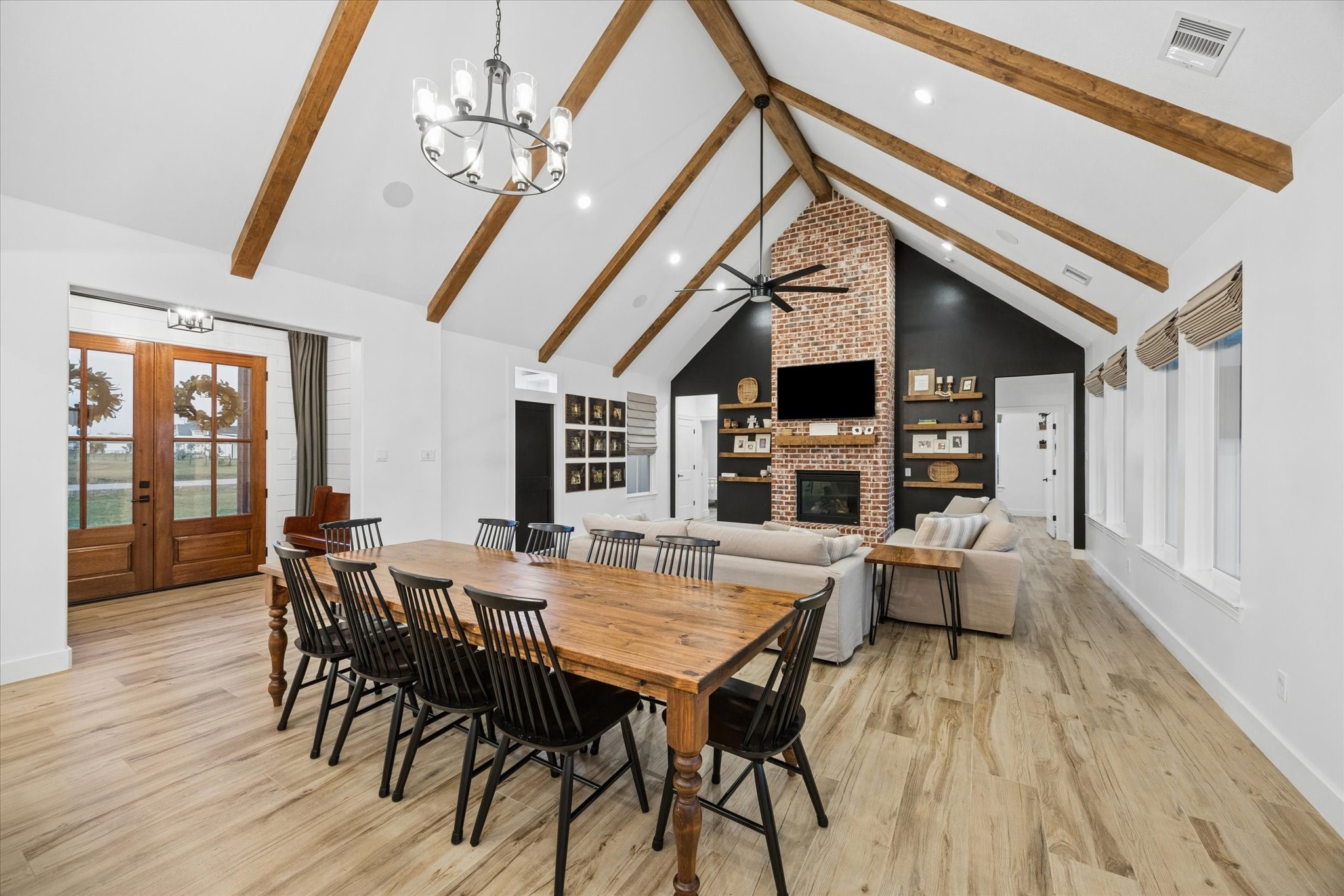 5131 Timber Ridge Drive Sealy, TX 77474 - Photo 7 of 50 Spacious open-concept living and dining area with vaulted ceilings and wooden beams. It features a brick fireplace, hardwood floors, and ample natural light from multiple windows.