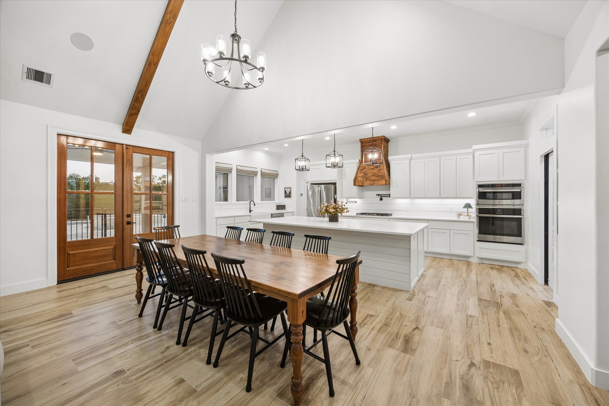 5131 Timber Ridge Drive Sealy, TX 77474 - Photo 8 of 50 This spacious, open-concept kitchen and dining area features high vaulted ceilings, elegant wood flooring, and modern fixtures. The large island, stainless steel appliances, and ample cabinetry offer functionality and style. French doors provide natural light and access to outdoor space.