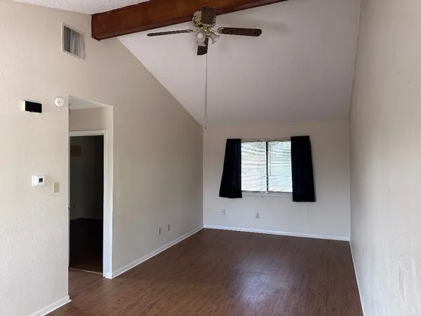 a view of an empty room with wooden floor and a window