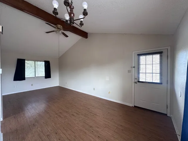 an empty room with wooden floor chandelier fan and windows