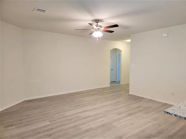a view of an empty room with wooden floor and a ceiling fan