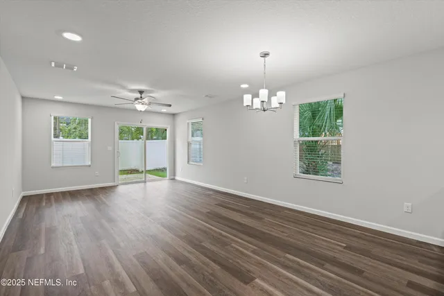 an empty room with wooden floor chandelier and windows