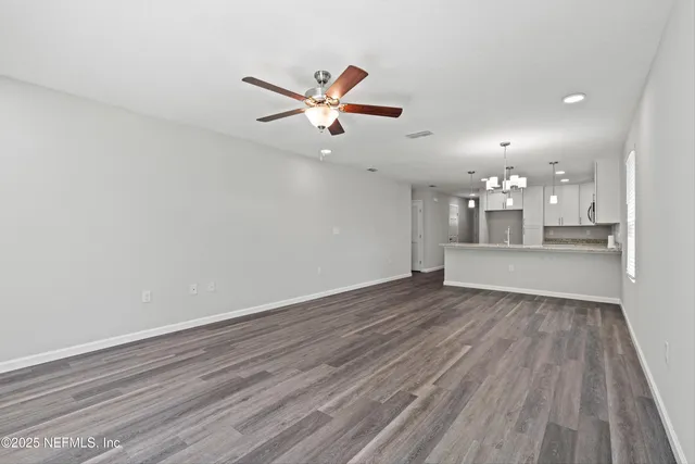 a view of an empty room with wooden floor and a ceiling fan