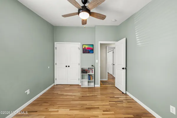 a view of an empty room with wooden floor and a ceiling fan