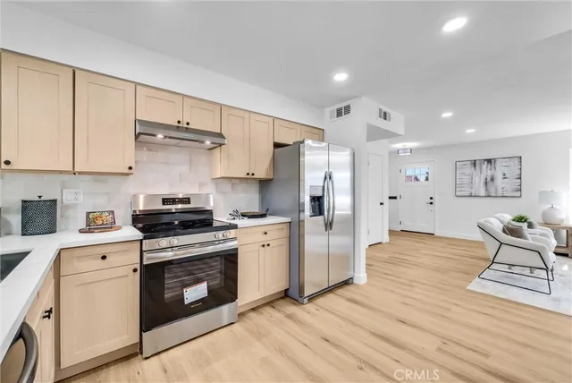 a kitchen with stainless steel appliances a stove a refrigerator white cabinets and wooden floors