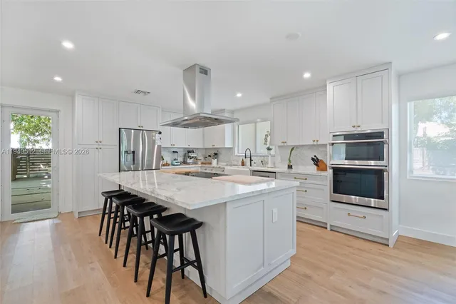 a kitchen with stainless steel appliances a microwave a stove a sink dishwasher a refrigerator and white cabinets with wooden floor