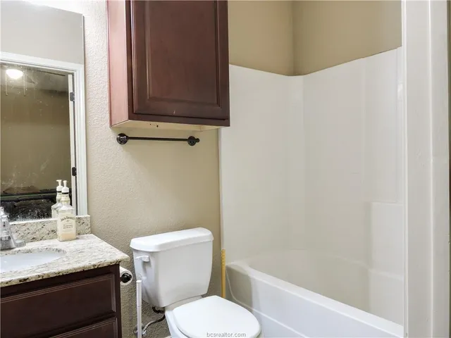 a bathroom with a granite countertop toilet sink and mirror