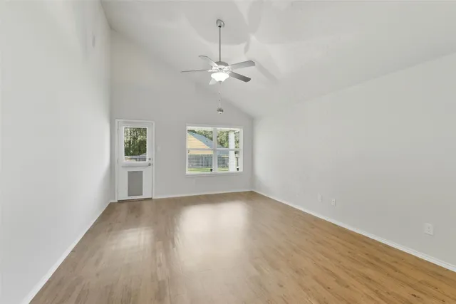 an empty room with wooden floor chandelier fan and windows