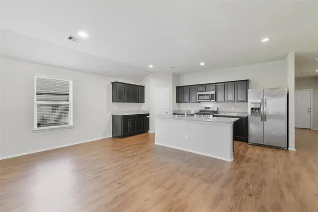 a view of kitchen with granite countertop refrigerator oven a sink dishwasher and white cabinets with wooden floor