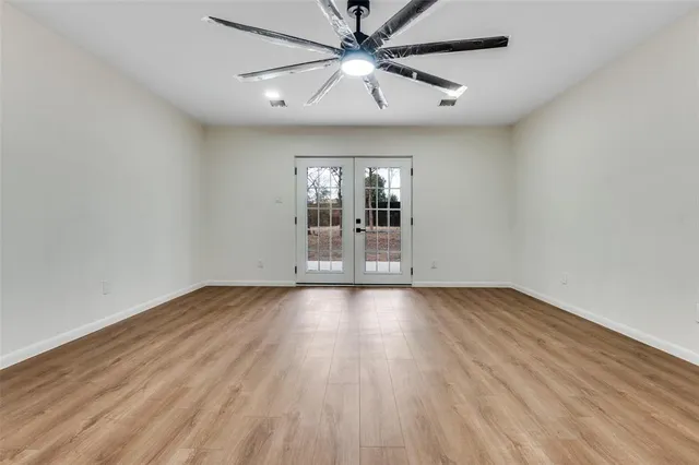 an empty room with wooden floor chandelier fan and windows