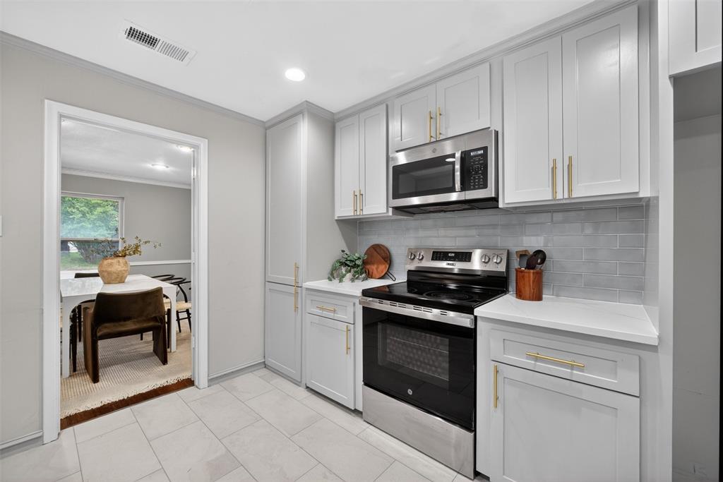 9660 Timberleaf Drive Dallas, TX 75243 - Photo 14 of 40 Bright kitchen featuring light gray cabinetry with gold-tone hardware, stainless steel appliances, a subway tile backsplash, and light-toned countertops