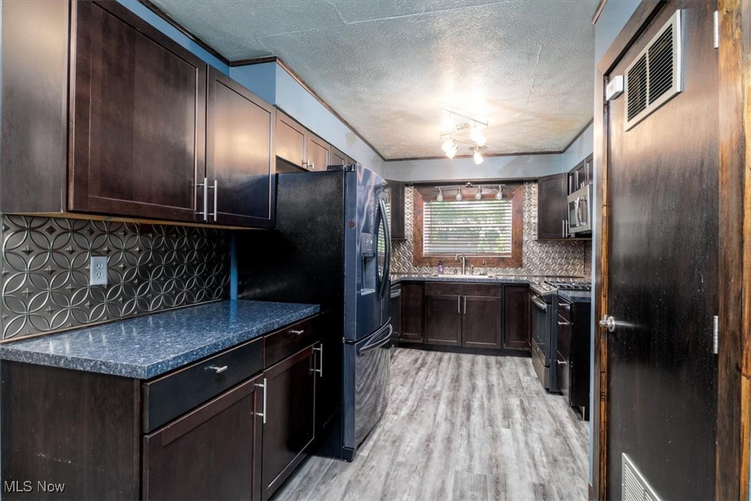 6401 West Ridgewood Drive Cleveland, OH 44129 - Photo 5 of 17 Kitchen with appliances with stainless steel finishes, a sink, backsplash, light wood-style floors, and dark brown cabinetry