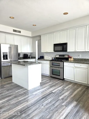 a large kitchen with granite countertop a sink a stove top oven and wooden floor