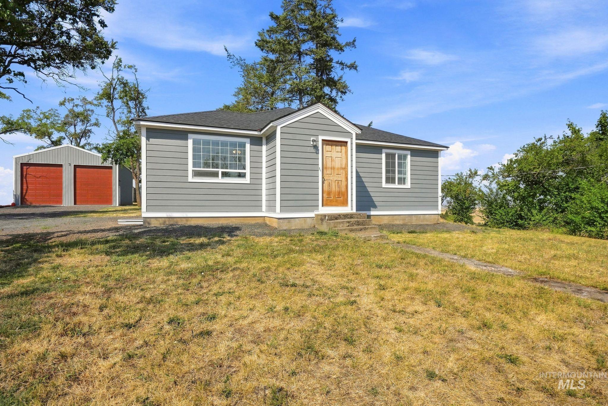 16078 Hoffman Road Kendrick, ID 83537 - Photo 4 of 47 Gray horizontal siding, white trim, wood entry door, dark shingle roof, and mature perimeter trees