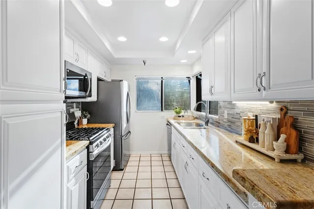 a kitchen with stainless steel appliances granite countertop a stove top oven a sink a refrigerator and white cabinets