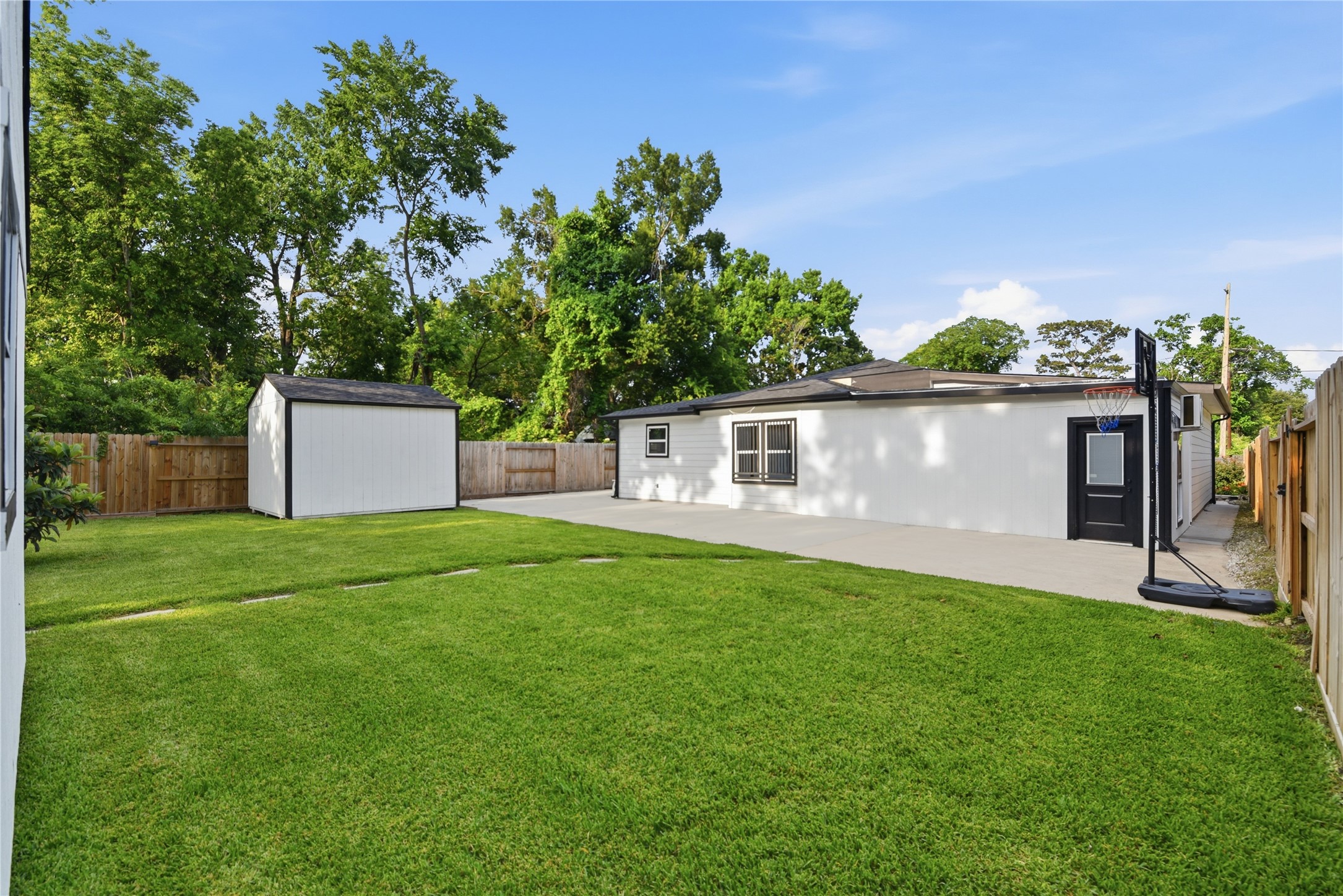 9403 Spaulding Street Houston, TX 77016 - Photo 44 of 50 Spacious backyard with lush green grass, a small storage shed, and a paved area perfect for outdoor activities. Enclosed by wood fencing for privacy.