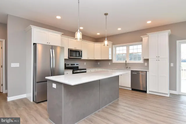 a kitchen with stainless steel appliances granite countertop a refrigerator a sink dishwasher a stove and white countertops with wooden floor