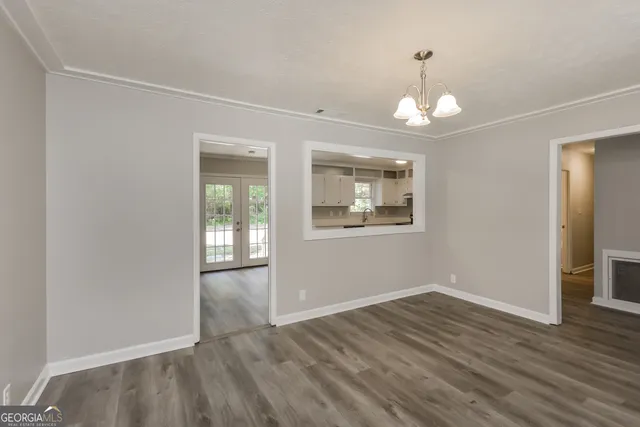 an empty room with wooden floor chandelier and windows
