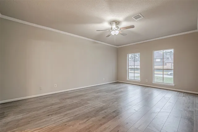 an empty room with wooden floor chandelier fan and windows