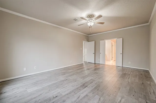 a view of an empty room with wooden floor and a chandelier fan