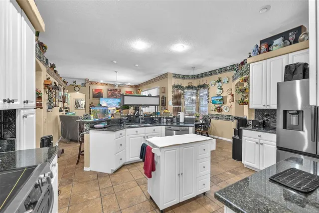 a kitchen with stainless steel appliances kitchen island granite countertop a refrigerator a stove top oven and a dining table with wooden floor