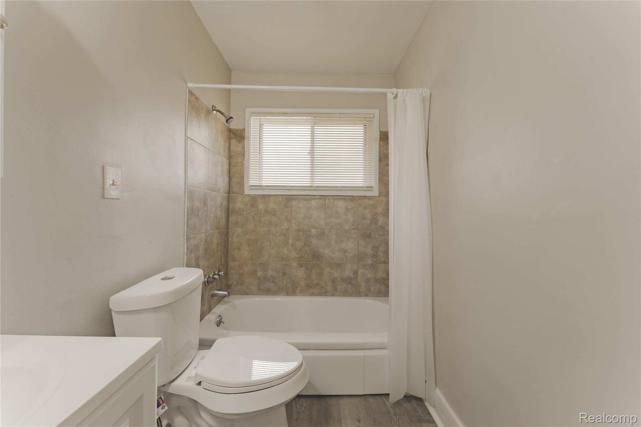 93 West Princeton Avenue Pontiac, MI 48340 - Photo 15 of 31 Bathroom featuring a shower-tub combination, ceramic tile surround, white toilet, and wood-finish flooring