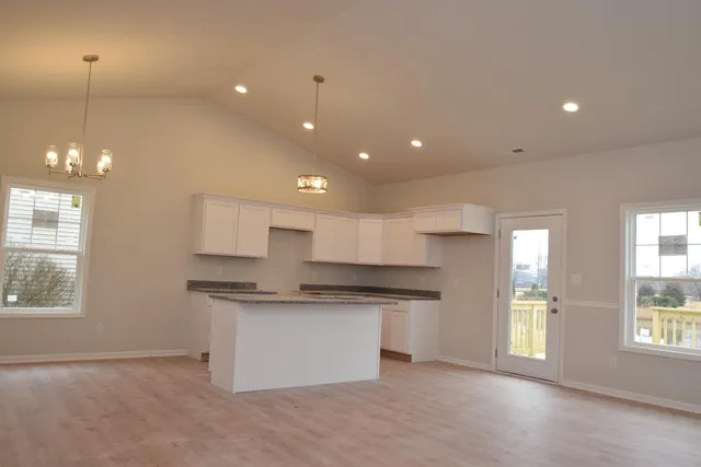 a open kitchen with kitchen island a sink dishwasher a refrigerator and white cabinets with wooden floor