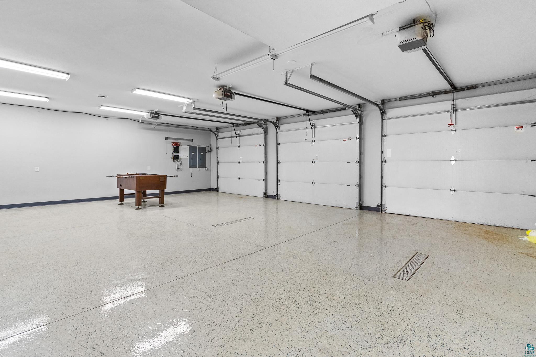 5163 Greenwood Road Duluth, MN 55804 - Photo 41 of 47 Spacious garage featuring three overhead doors, glossy epoxy flooring, fluorescent lighting, and a utility panel